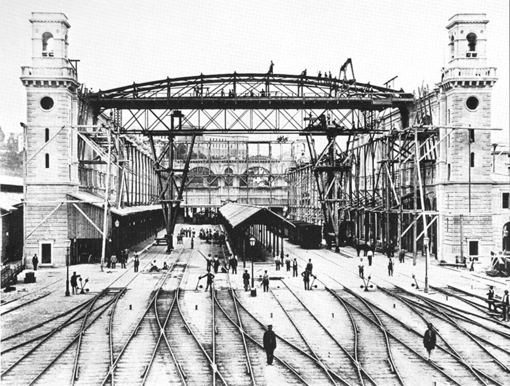 Der Bahnhof während seines Baus. Beachte, dass die Gleise damals durch die gesamte Halle führten – heute ist diese weitgehend leer.