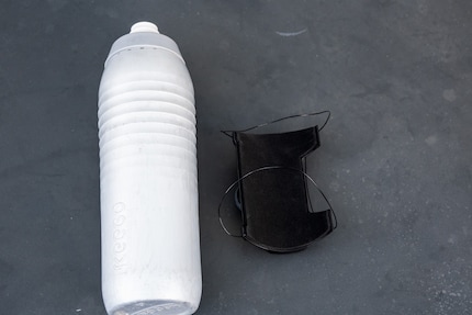 Die Trinkflasche kommt durch die beiden Laschen und wird anschliessend mit dem Drehknopf festgezogen.